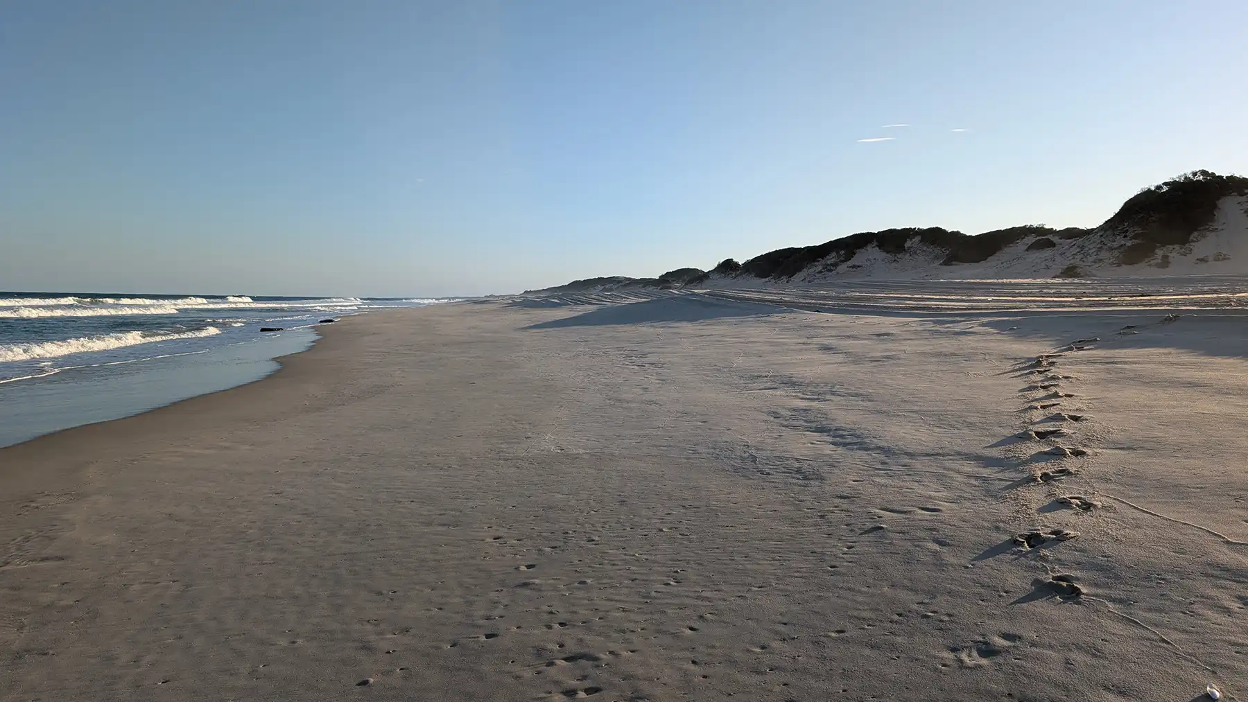 Golden afternoon light washes over the quiet shores of Calanga, where gentle waves meet untouched sands and the day drifts softly toward sunset.