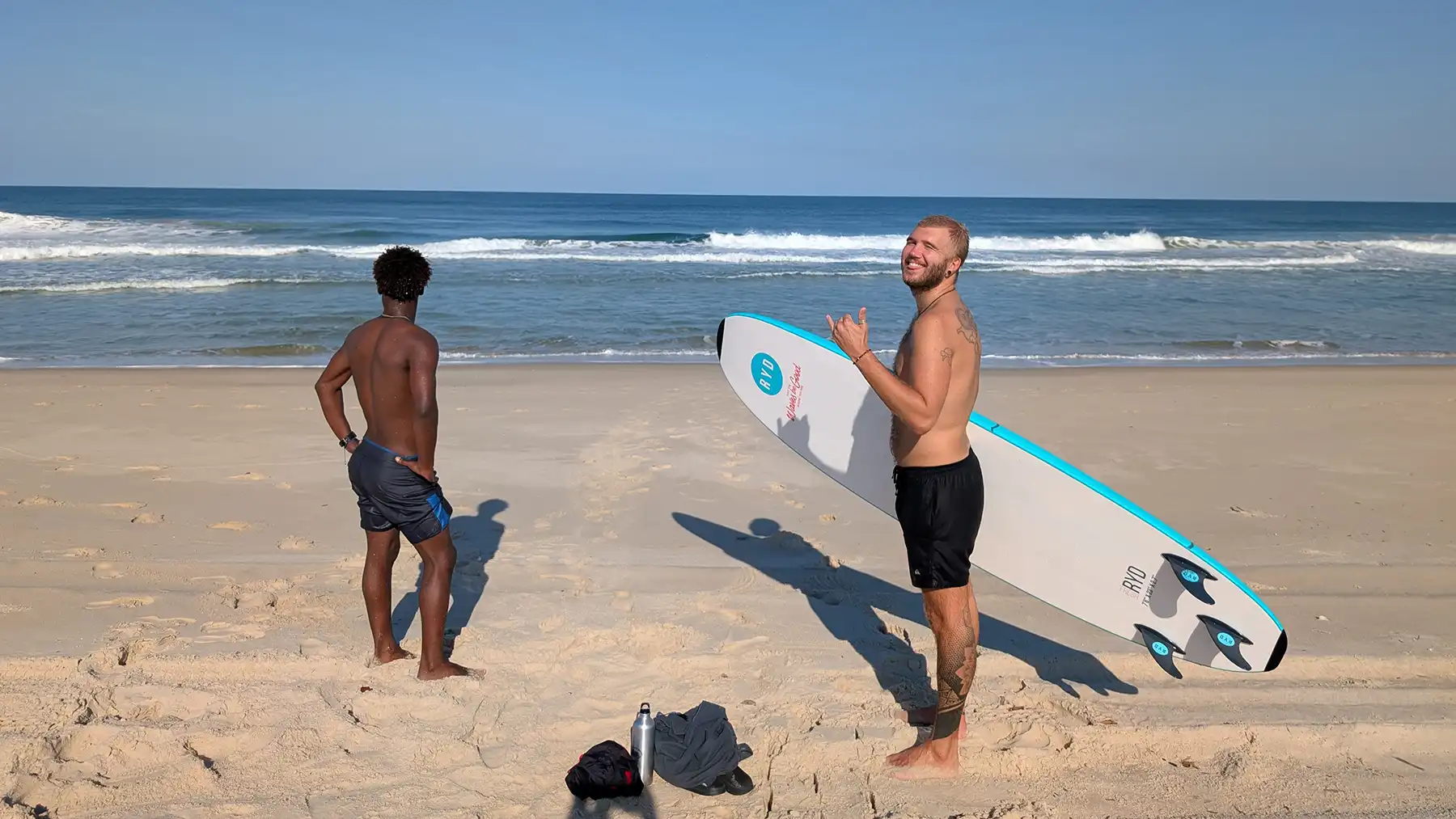 Two surfers pause on the quiet sands of Dune Beach Hostel, watching the late-afternoon swell roll in—anticipating the perfect moment to paddle out.